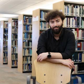 Male student leaning on a chair in a library