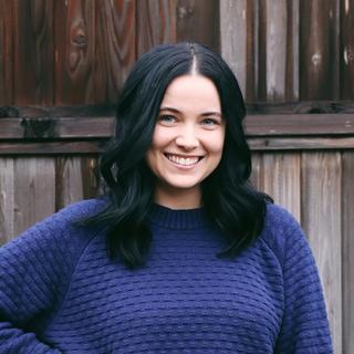 Alisha wearing a blue sweater standing in front of a fence