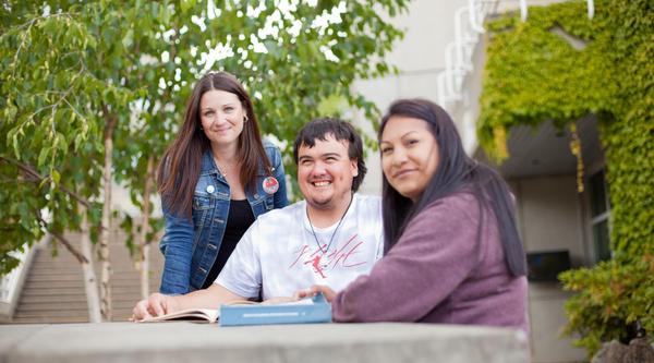 Three students chat around a table outside