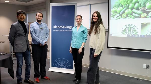 Four students, two males and two females standing beside a banner