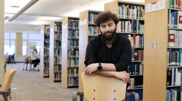 Male student leaning on a chair in a library