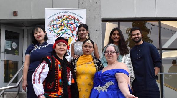 A group of people in various cultural attire standing in front of a WorldVIU sign on the steps of the VIU library