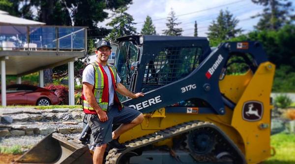 Jesse Anderson standing outside in front of one of his machines on a sunny day.