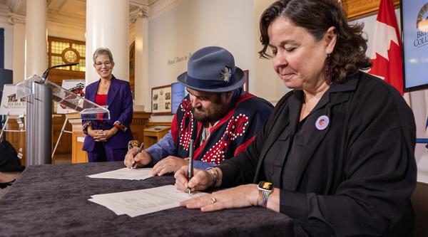 Two people sign papers while a third in the background looks on