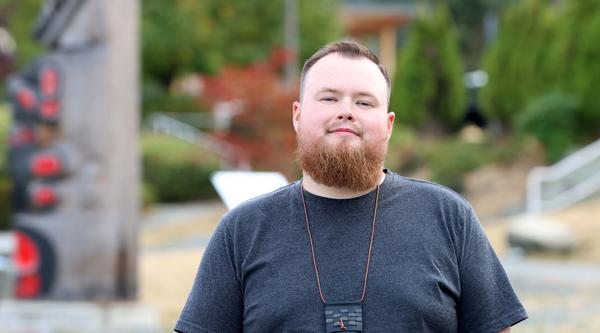 Portrait of Aaron Moore in front of totems at VIU Nanaimo campus