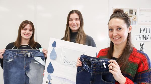 Two students hold up jeans and another holds up a poster.