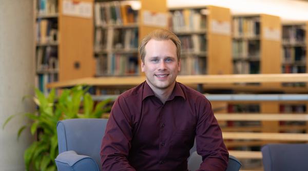 Chris Shanks sits on a blue chair in a library.