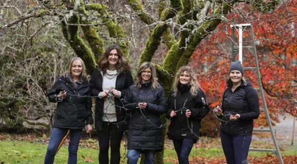 Five women hold Christmas lights at Milner Gardens with a ladder behind them
