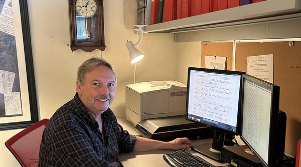 Stephen Davies sits at his computer with a digitized letter on the screen