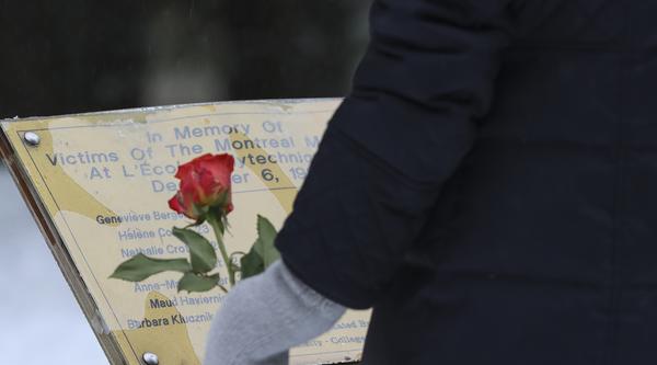A person holding a rose stands in front of the Jardin des Quartorze garden memorial.