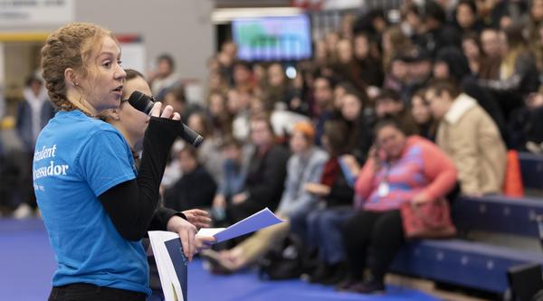 A student speaks into a microphone in front of a crowd
