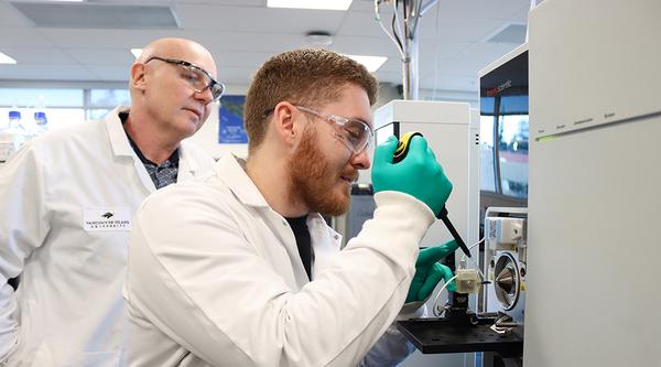 Dr. Chris Gill observes as Lucas Abruzzi puts a sample in the mass spectrometer.