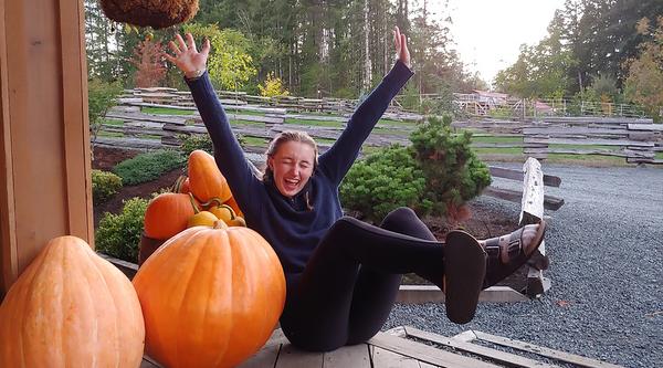 Girl poses with arms spread next to pumpkins