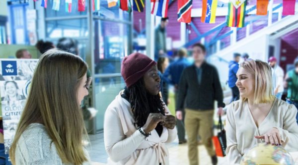 Three woman standing and chatting in front of a table on which sits two globes.