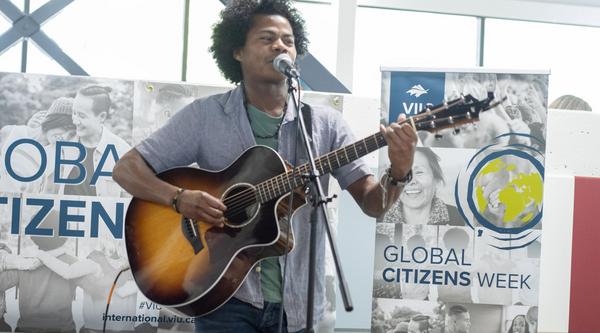 Student sings and plays guitar with Global Citizens Week banners behind him