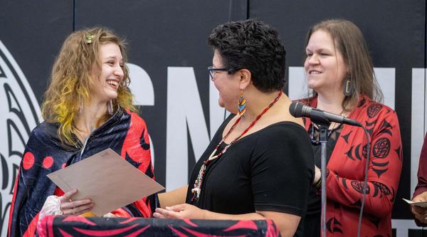 A student receives a folder from a woman, with another woman watching in the background