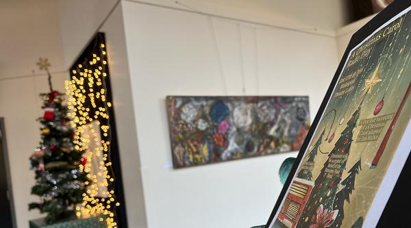 A Christmas Carol poster sits on a stand in front of a Christmas tree.