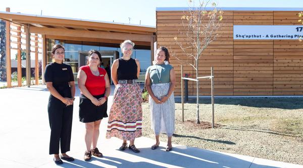Four people stand in front of Shq'apthut: A Gathering Place