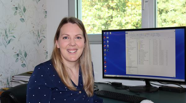 VIU Psychology Professor Becky Earhart sitting at her desk in front of a computer screen and smiling at the camera.