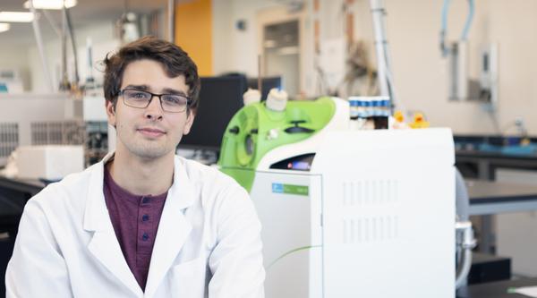 Joseph Monaghan sits in a VIU Chemistry lab, wearing a white lab coat.