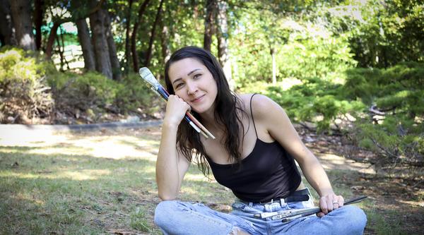 Kashmir Lesnick-Petrovicz sits on the ground and holds paint brushes in her hands.