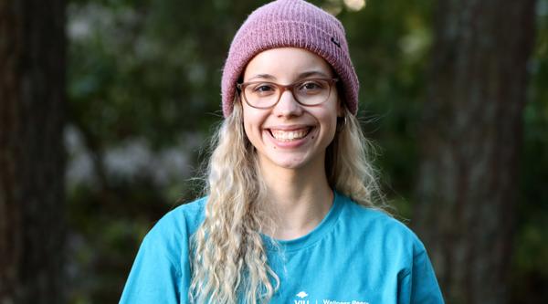 Portrait photo of Kennedy Ordano smiling at the camera with a forest background