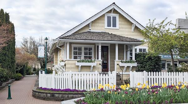 A building painted yellow with a white picket fence around it and a flower box with tulips out front.