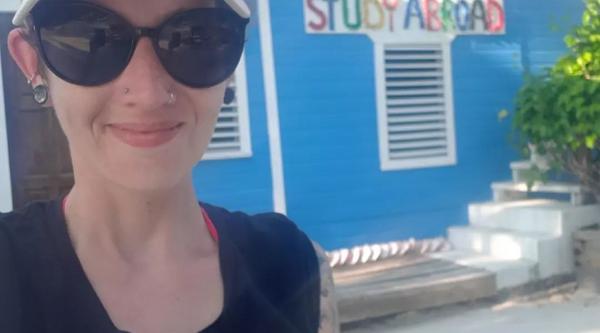 Melanie stands in front of the Tobacco Caye sign, which reads Study Abroad underneath it
