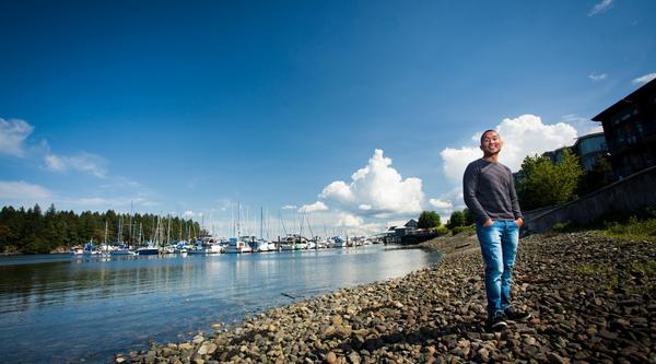 A man stands in the foreground with the waterfront and a marina full of boats behind him