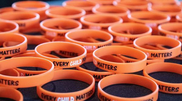 Dozens of orange bracelets that read Every Child Matters