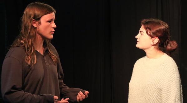 Two actors face each other on stage while rehearsing a scene.