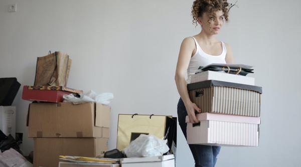 Student carrying boxes with more piled behind her, looking anxious