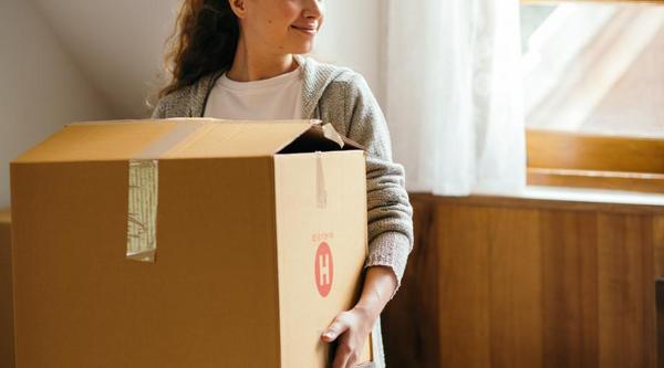 A girl holds a moving box while standing in a bedroom