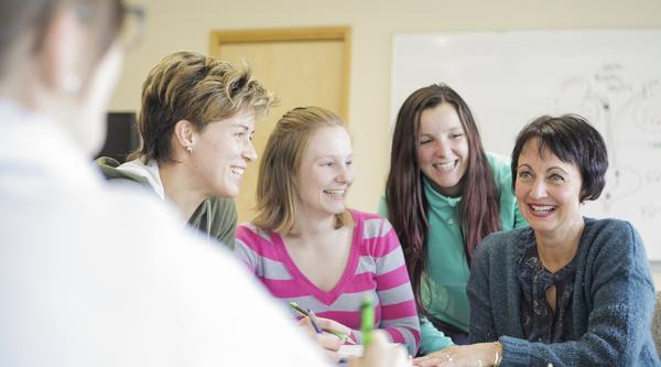 Four students and a faculty member sit at a table together, smiling.