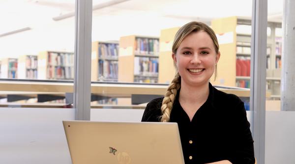 VIU Psychology student Cala Annala sitting at a desk with an open MacBook in front of her
