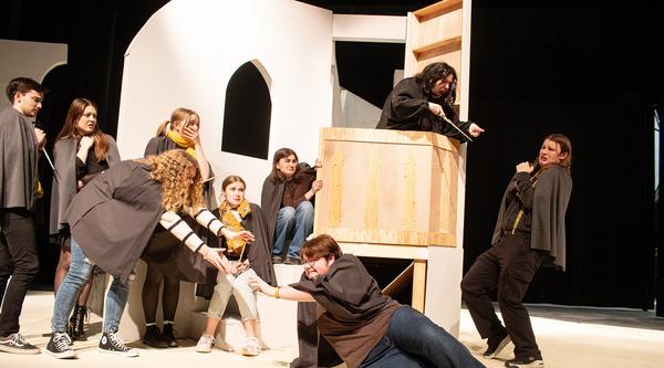 Six actors on the left reach out to one of their cast mates while another stands in fear on the right.