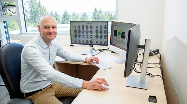Sandy sits at his desk with images of brains open on one screen