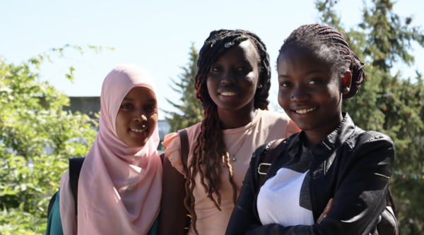 Facing the camera and standing from left to right are refugee students Hanan Ali Abdi, Nyagua Deng Goch, and Daniella (Sifa) Mukenge