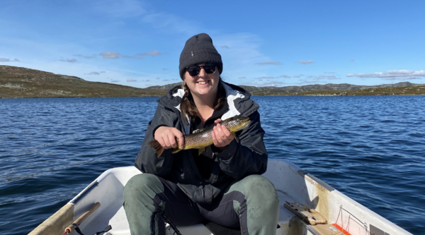 Sarah Osborne sitting in a boat holding a fish and smiling at the camera