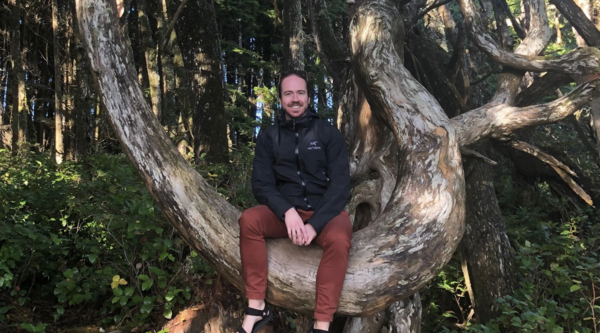 Dr. Michael Asmussen sitting in a tree and smiling at the camera.