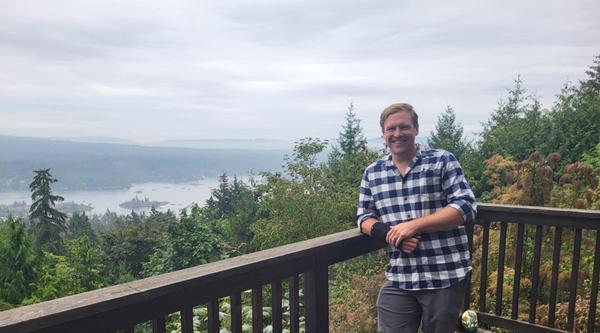 Stephen Hextall leans against a railing with trees and a lake in the background.