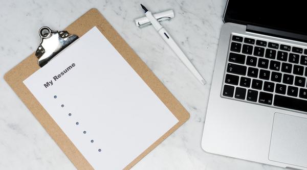 A clipboard the says "My Resume" with bullet points rests next to a laptop 