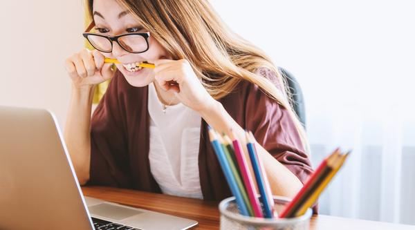 Girl sitting looking at laptop and biting a pencil