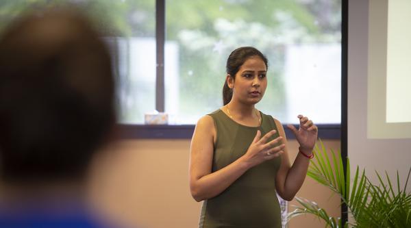 A student wearing a green dress stands in front of audience members and discusses their research during the 2019 CREATE Conference.