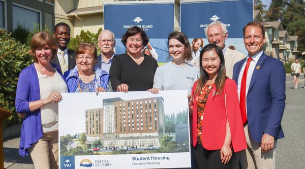 Group photo of people standing with a rendering of the new student housing building