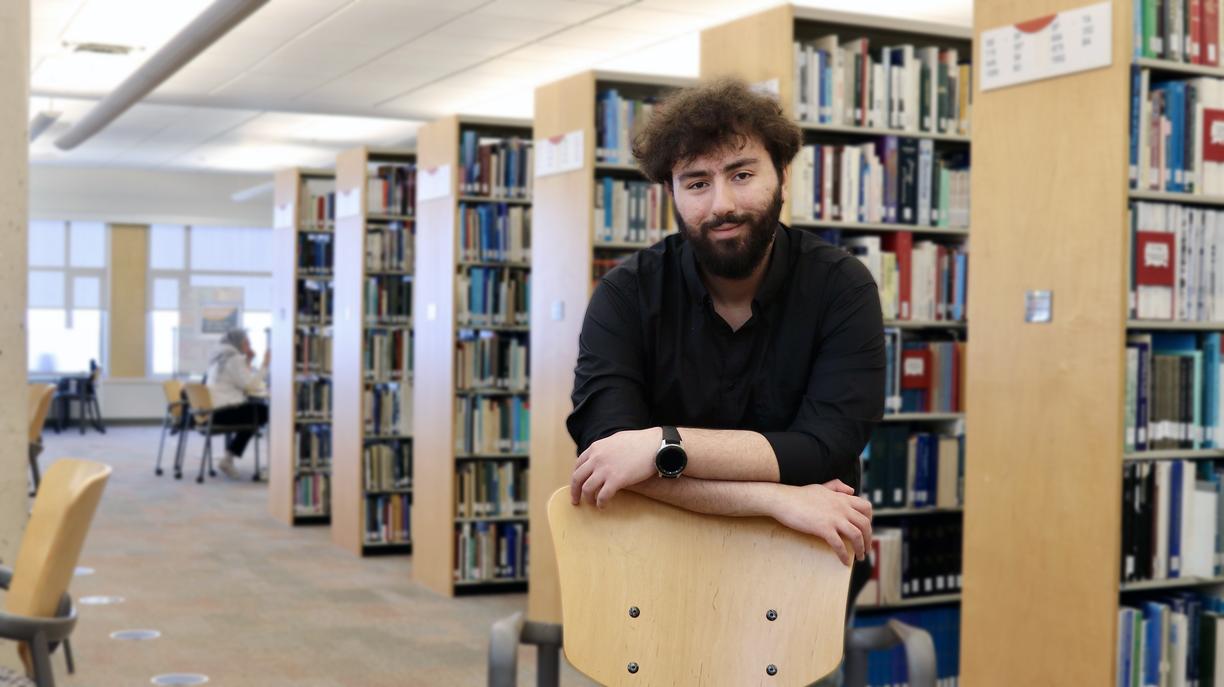 Male student leaning on a chair in a library