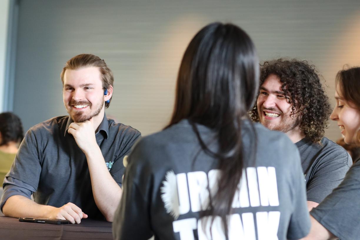 Three students wearing Urchin Tank T-Shirts talk while sitting at a table