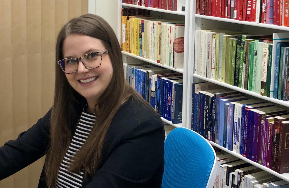Dr. Whitney Wood sits at a desk with a shelf of books behind her.