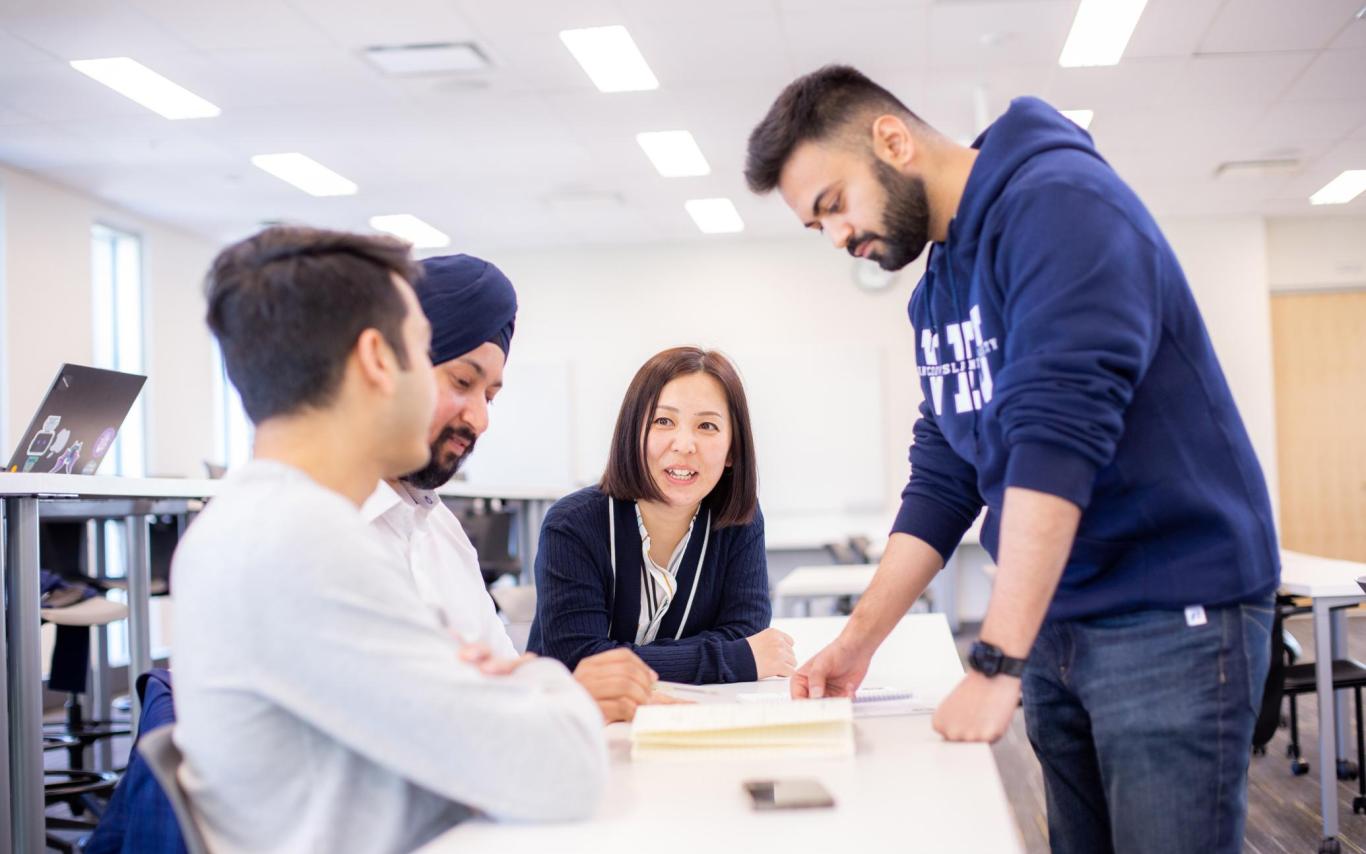 Four students look at a textbook together around a table