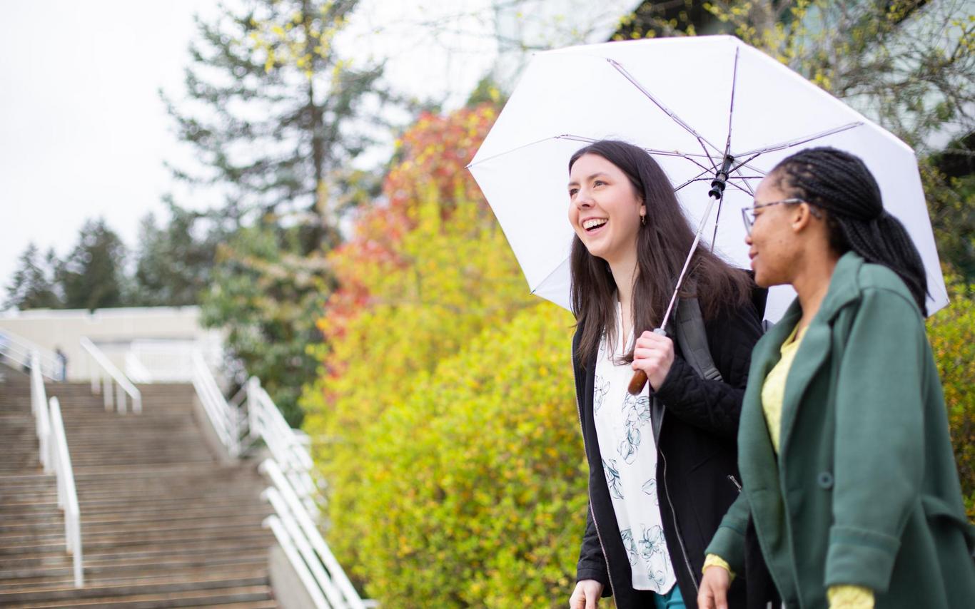 Two students walk near the stairs at VIU, one carries an umbrella
